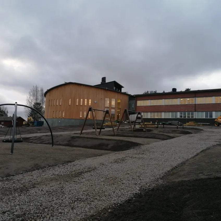 Skolgårdens lekplats med jämn och fin mark, med en grusväg som går mot den nybyggda skolan.