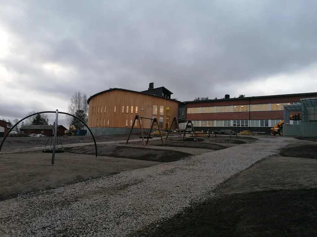 Skolgårdens lekplats med jämn och fin mark, med en grusväg som går mot den nybyggda skolan.